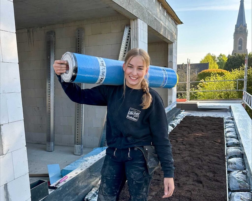Junge Dachdeckerin mit einer Materialrolle auf der Schulter